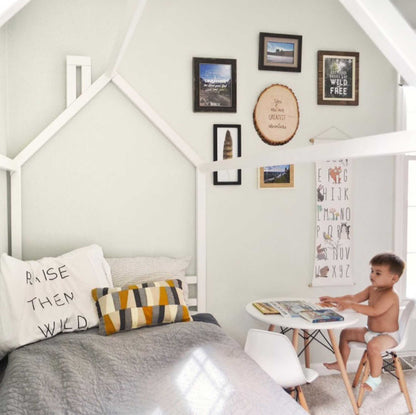 A boy's room with a Kids' house bed on legs with a headboard and footboard and framed pictures.