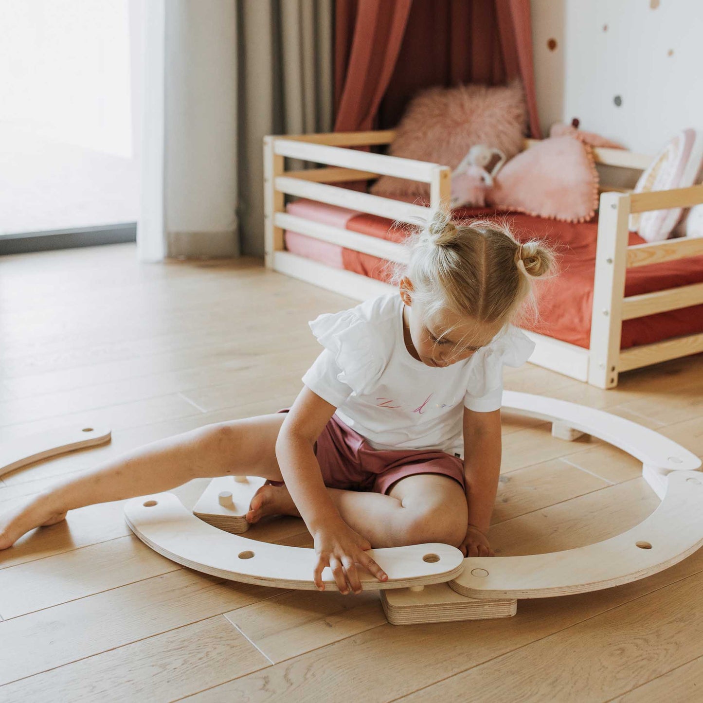 A little girl, on her first or second birthday, happily playing with a set of round balance beams in a room.