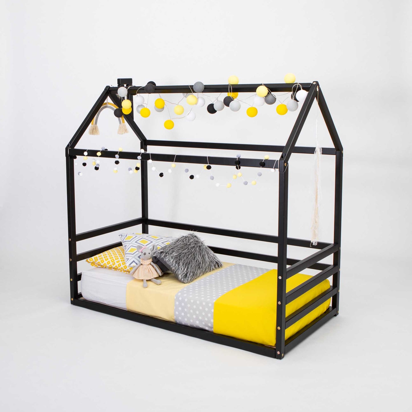 A black low kids' house-frame bed adorned with yellow pom poms.