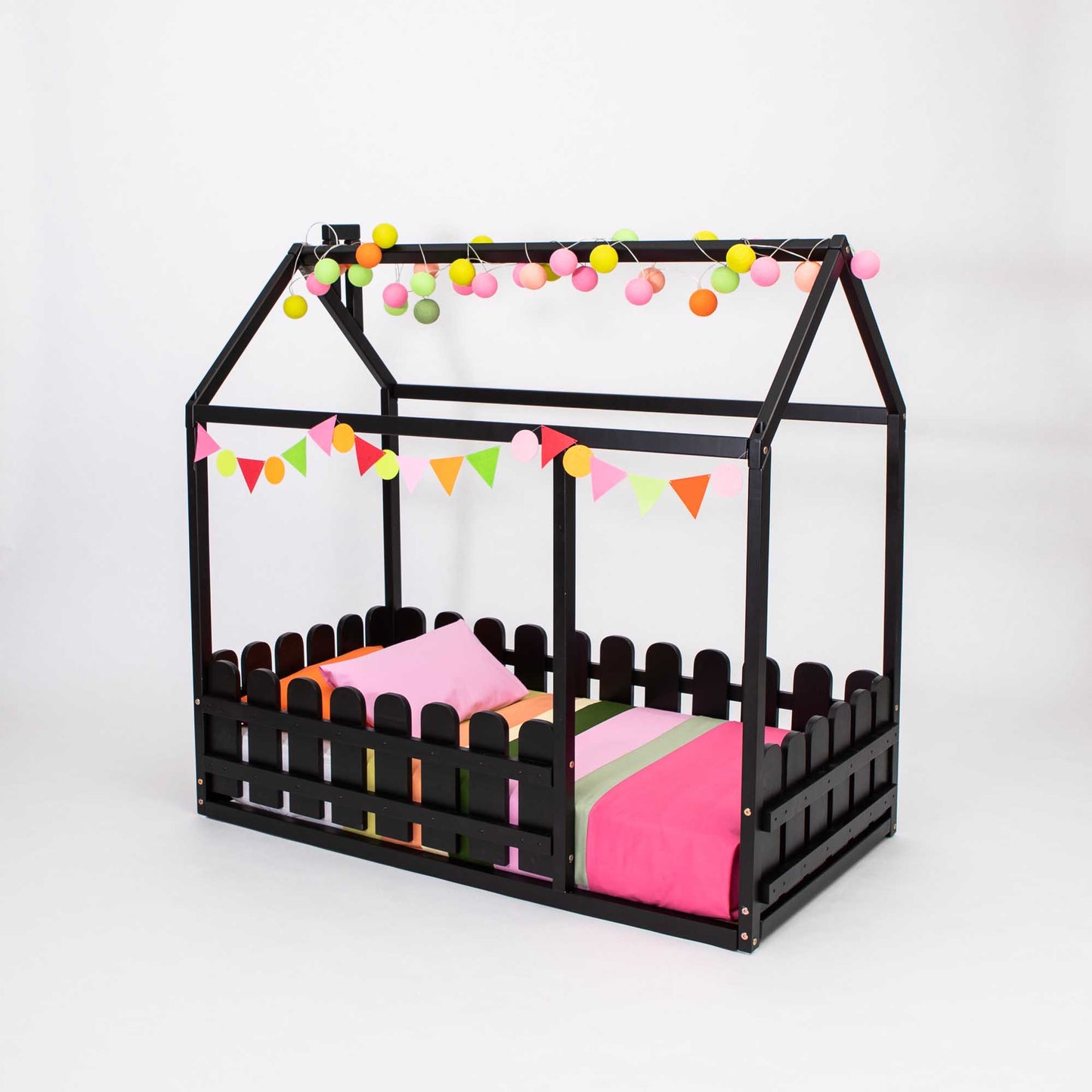 A black platform house bed with a picket fence and pink and black decorations.