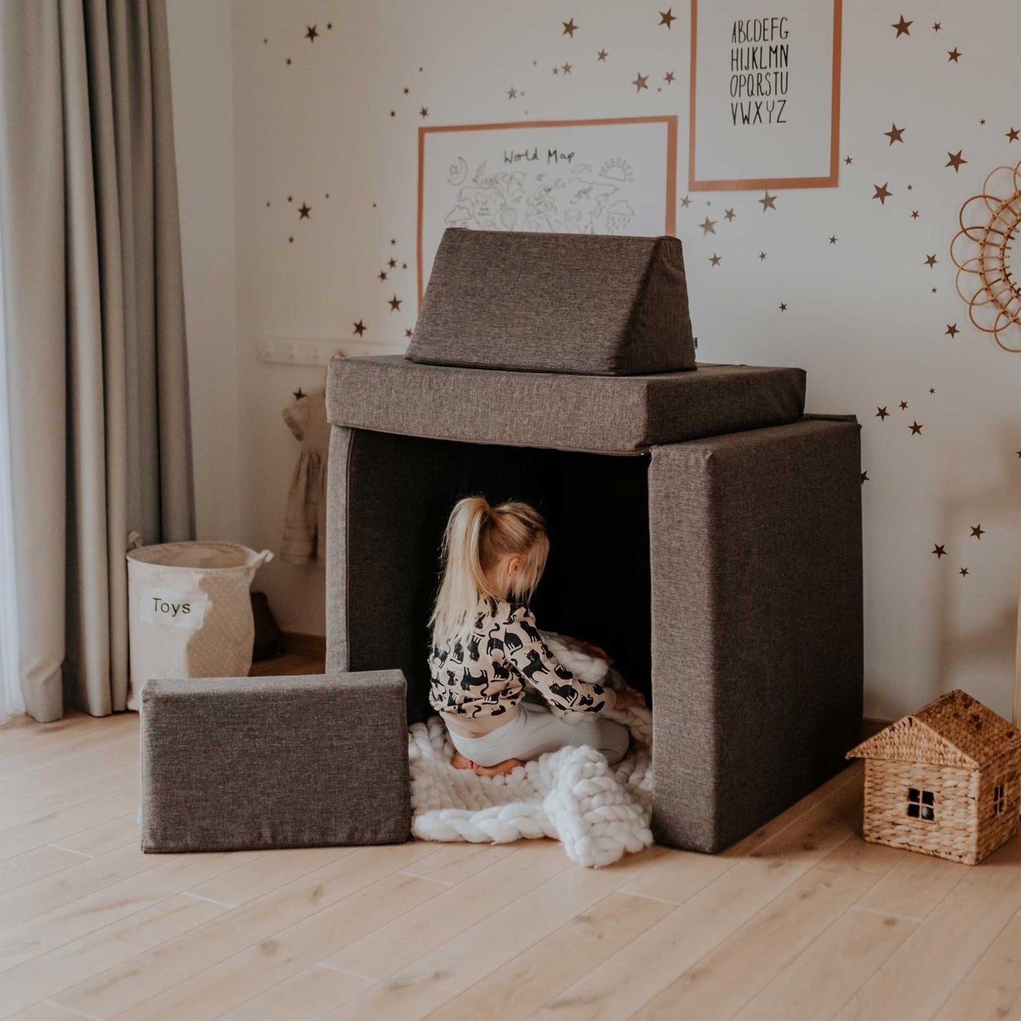A little girl sitting in a play house in her room, surrounded by a Sweet HOME from wood activity play couch set for kids.