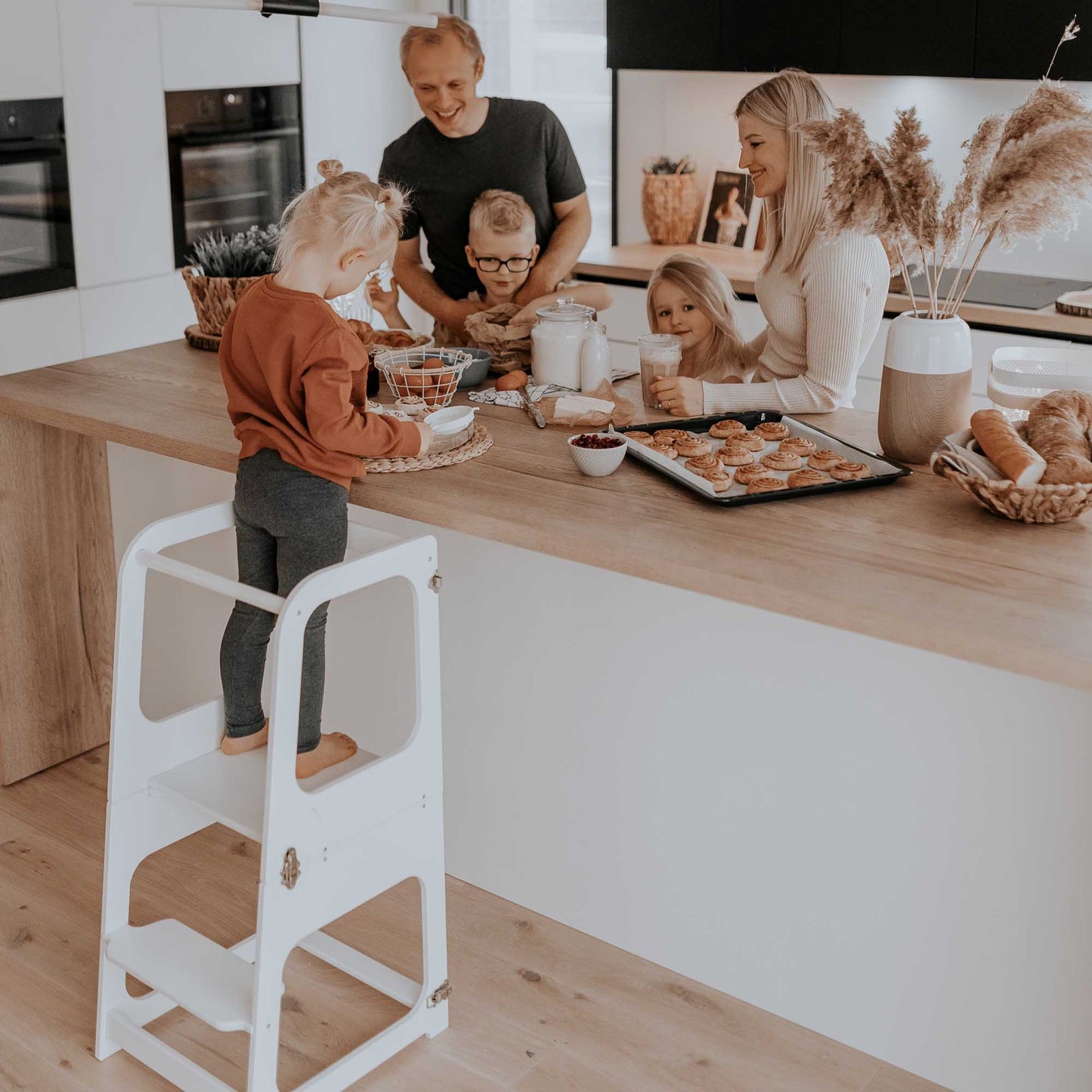 A family of kids is standing on a 2-in-1 Convertible kitchen tower - table and chair in the kitchen.