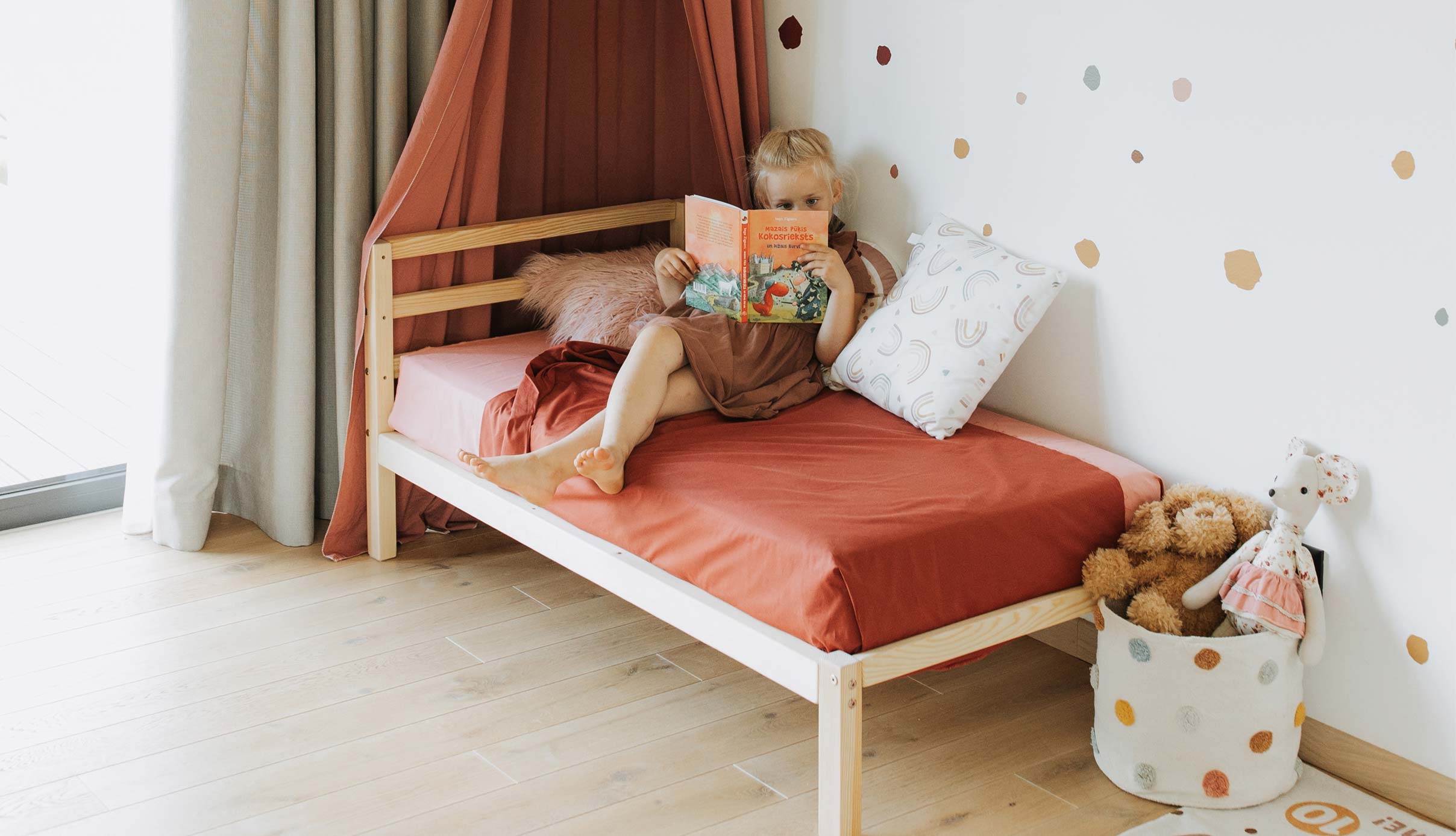 A little girl is reading a book on her bed.