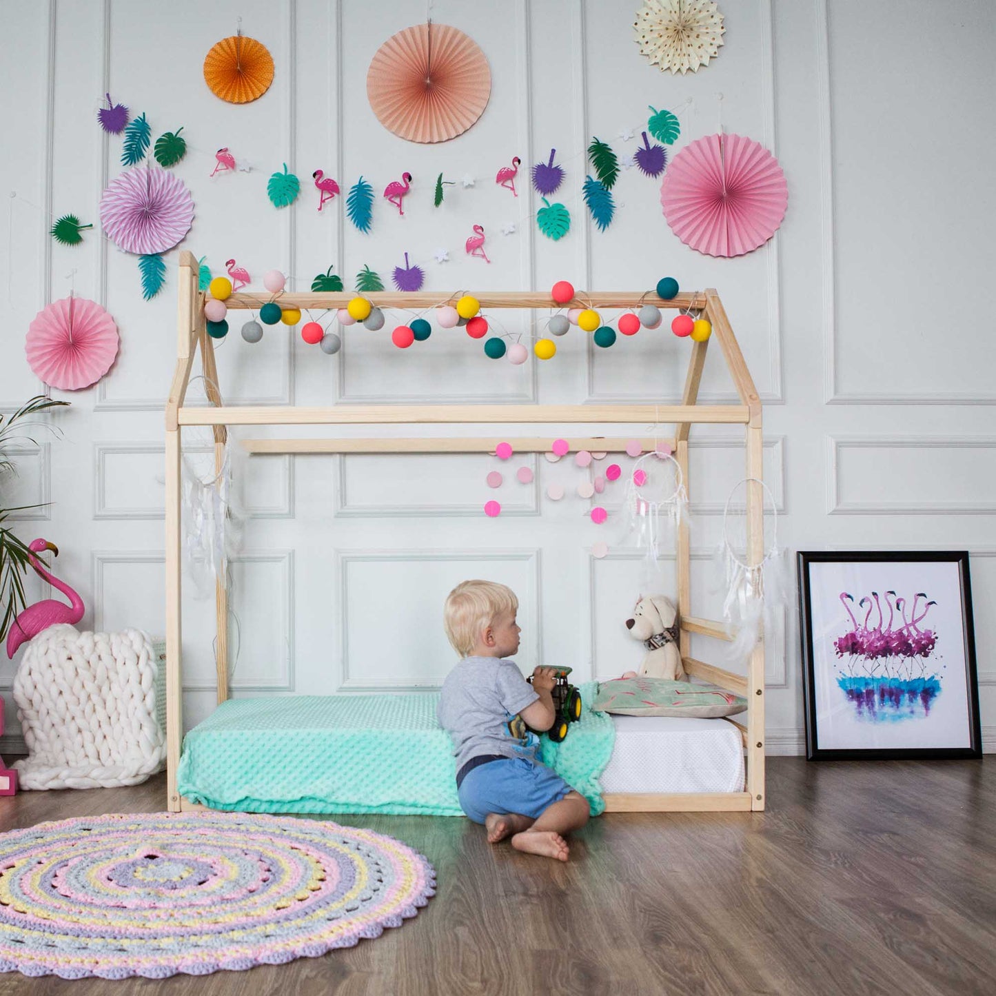 A child is playing on a Sweet Home From Wood Children's house bed with colorful pom poms.