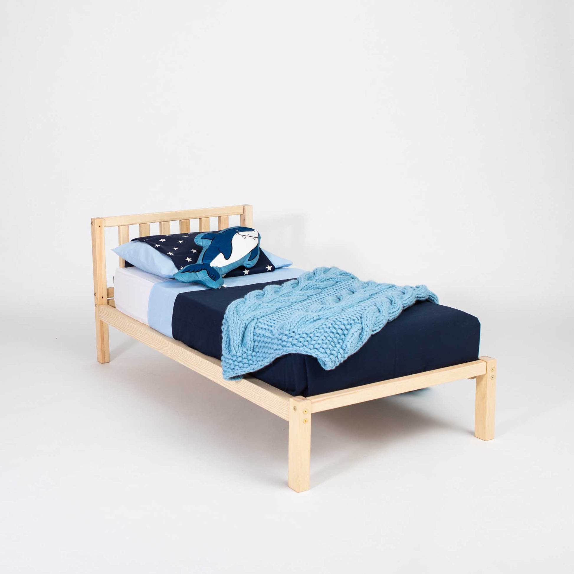 A Sweet Home From Wood 2-in-1 toddler bed on legs with a vertical rail headboard made of solid pine or birch wood, with a blue blanket on top.