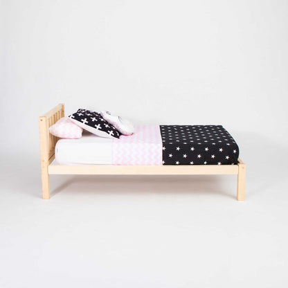 A Sweet Home From Wood 2-in-1 toddler bed on legs with a vertical rail headboard with a pink and black polka dot cover.