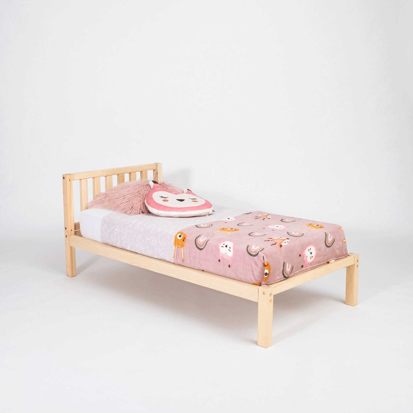 A small Sweet Home From Wood 2-in-1 toddler bed on legs with a vertical rail headboard, with a pink and white owl blanket.