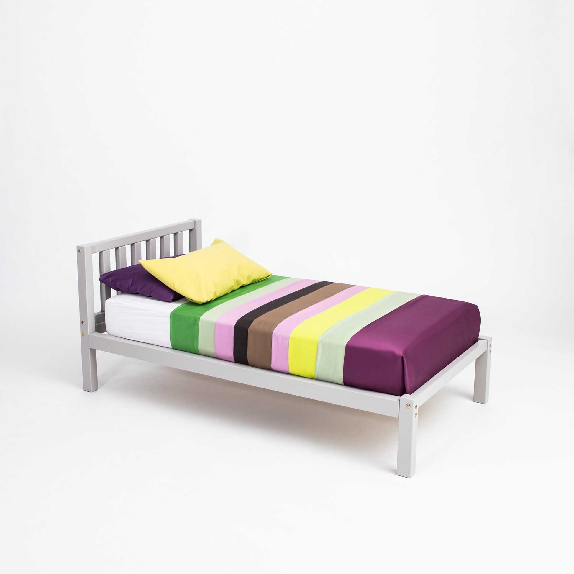 A Sweet Home From Wood 2-in-1 toddler bed on legs with a vertical rail headboard with a colorful striped sheet on it.