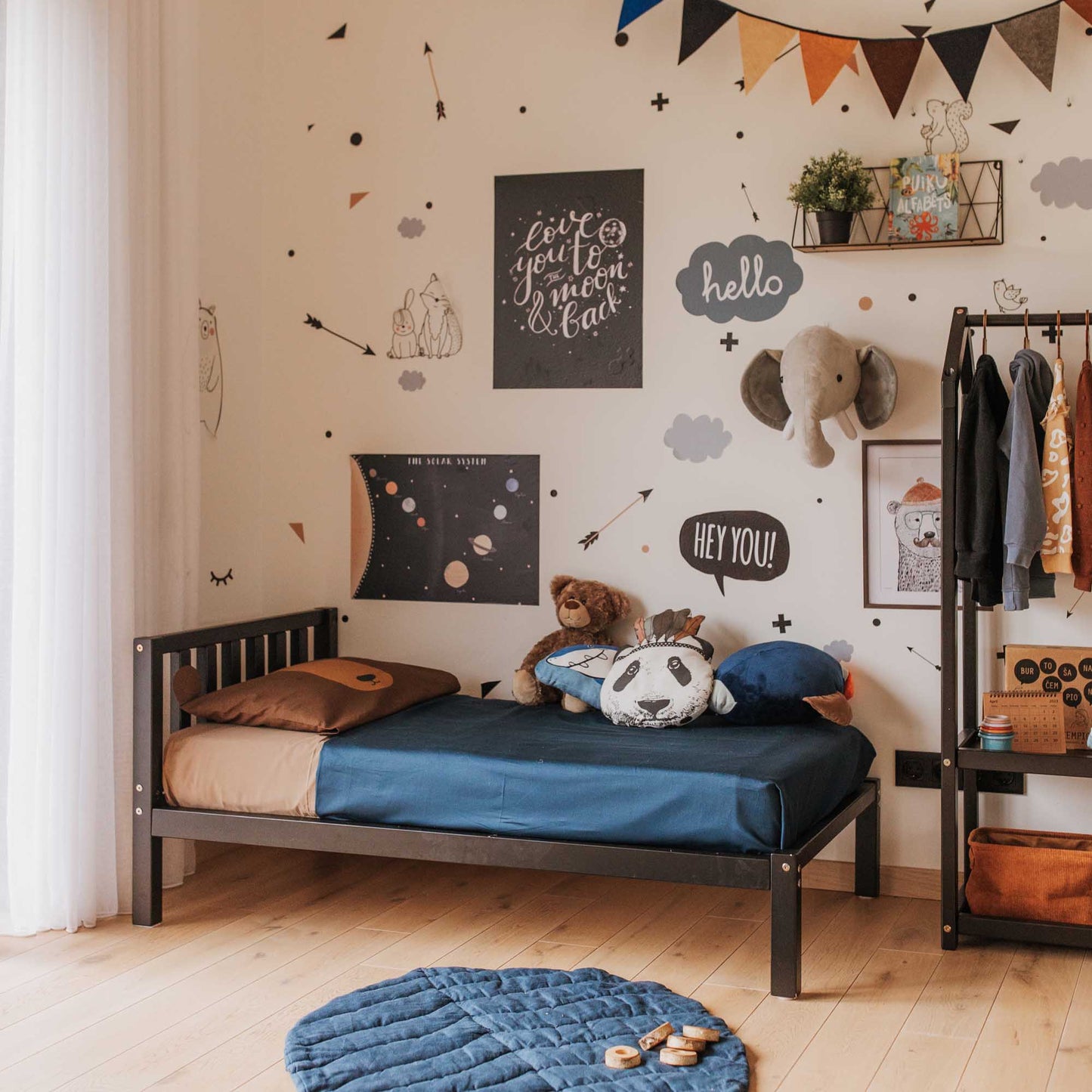 A Montessori-inspired boy's room with a Sweet Home From Wood 2-in-1 toddler bed on legs with a vertical rail headboard and a bedside table.