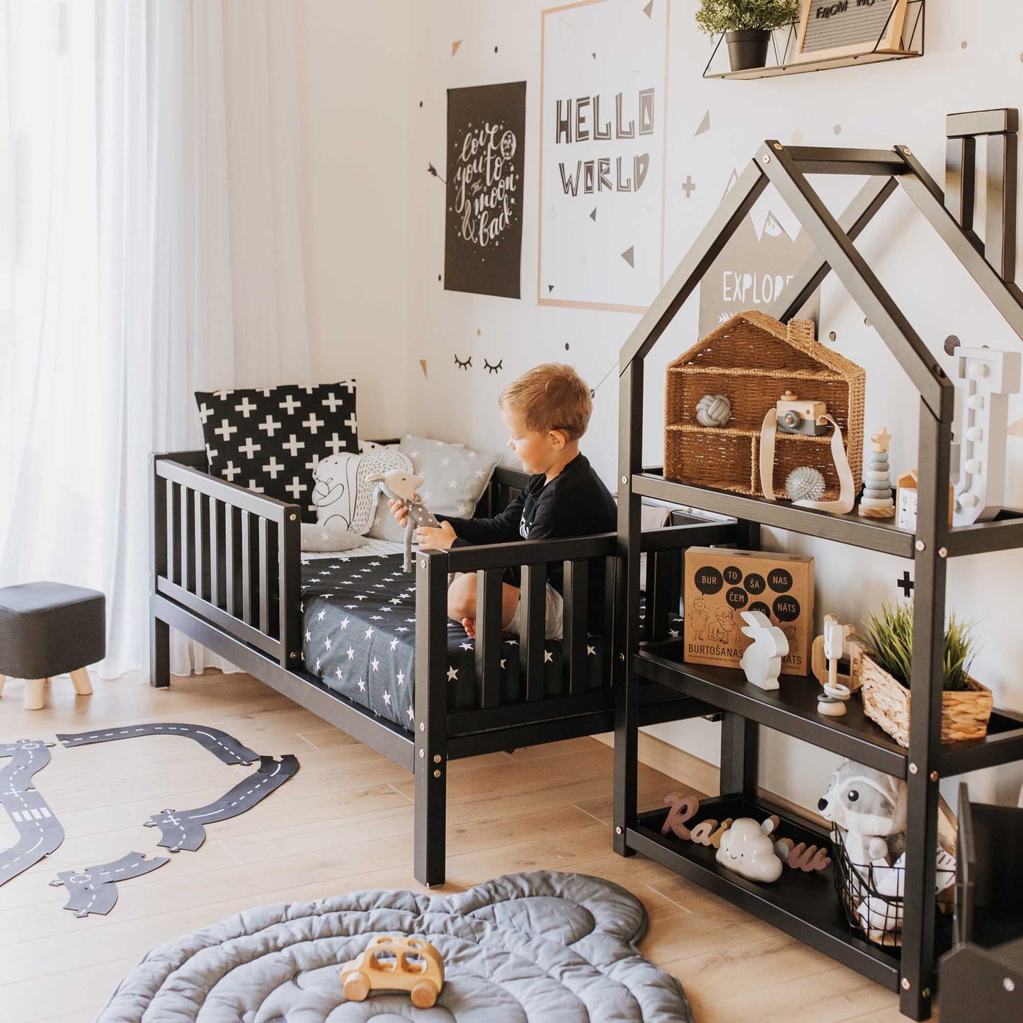 An independent sleeping space designed for a boy with a Sweet Home From Wood toddler bed on legs with a fence and a black and white rug.