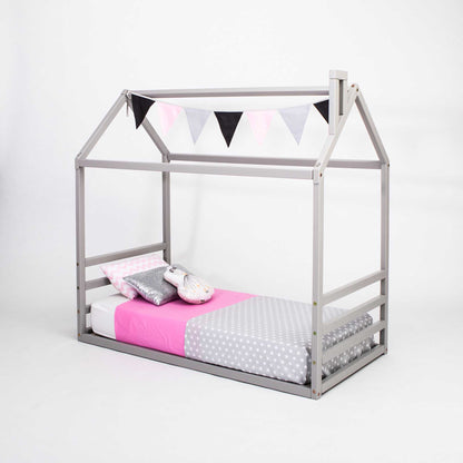 A floor house-frame bed with a horizontal headboard and footboard with a grey frame and pink and grey bedding.