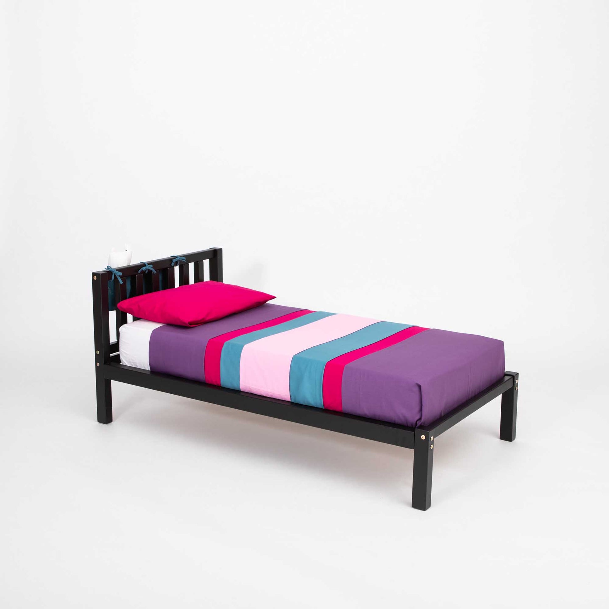 A black Kids' bed on legs with a headboard and a pink and purple striped sham, perfect for children seeking independence sleeping in a solid wood Montessori-style frame, from Sweet Home From Wood.