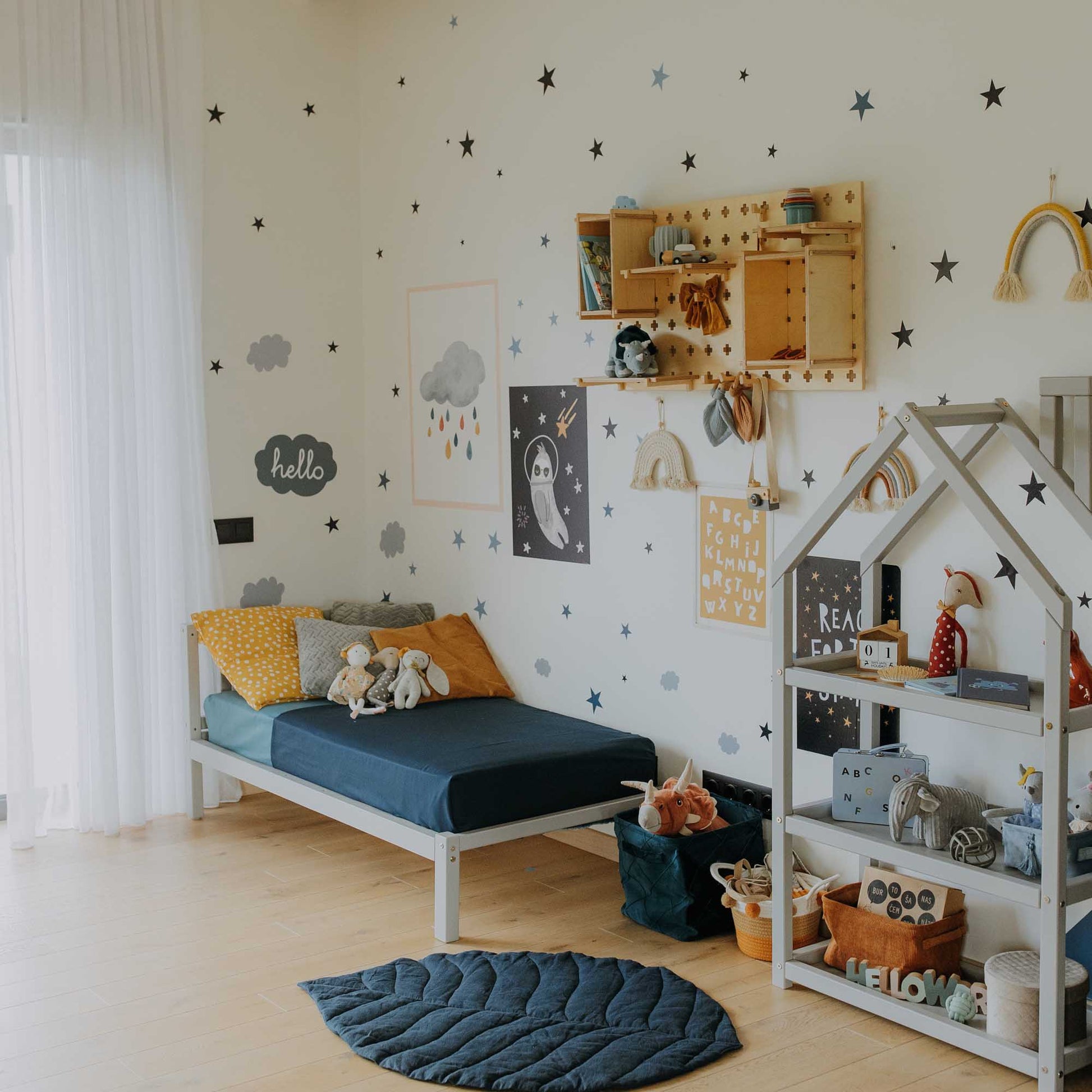 A Montessori-inspired child's room with a Sweet Home From Wood kids' bed on legs with a headboard, a bedside table, and a star wall.