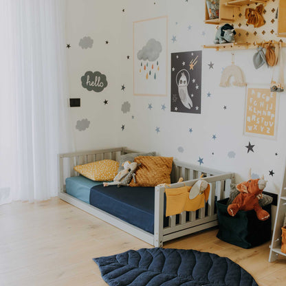 A child's room with a Sweet Home From Wood 2-in-1 toddler bed on legs with a 3-sided vertical rail and a chair.
