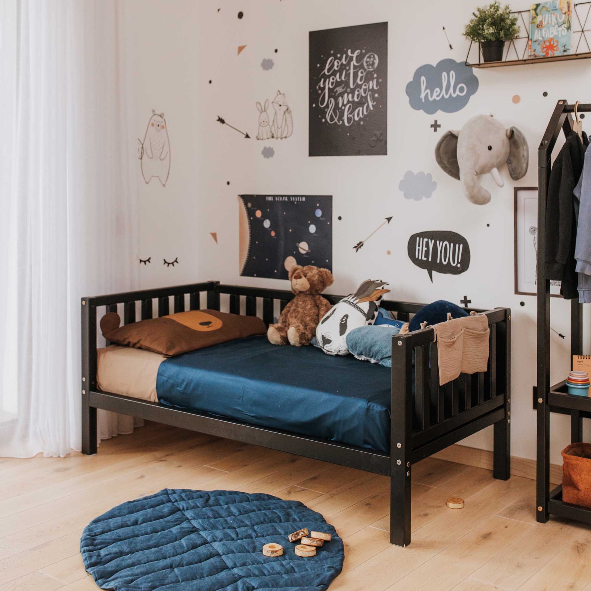 A toddler's room with a Sweet Home From Wood 2-in-1 toddler bed on legs with a 3-sided vertical rail and stuffed animals.