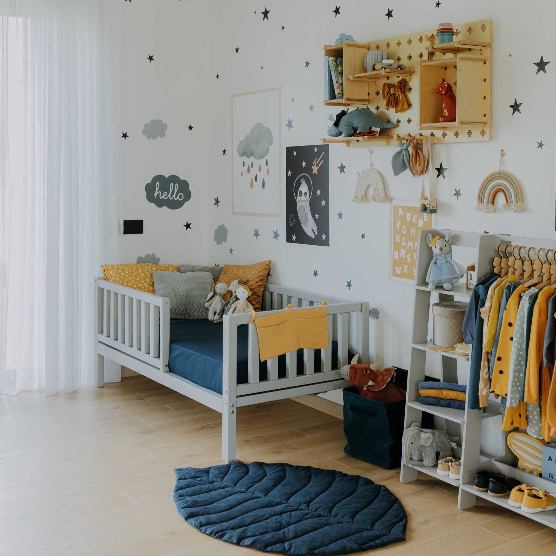 A child's room with a yellow and blue theme featuring a Sweet Home From Wood toddler bed on legs with a fence for independent sleeping.