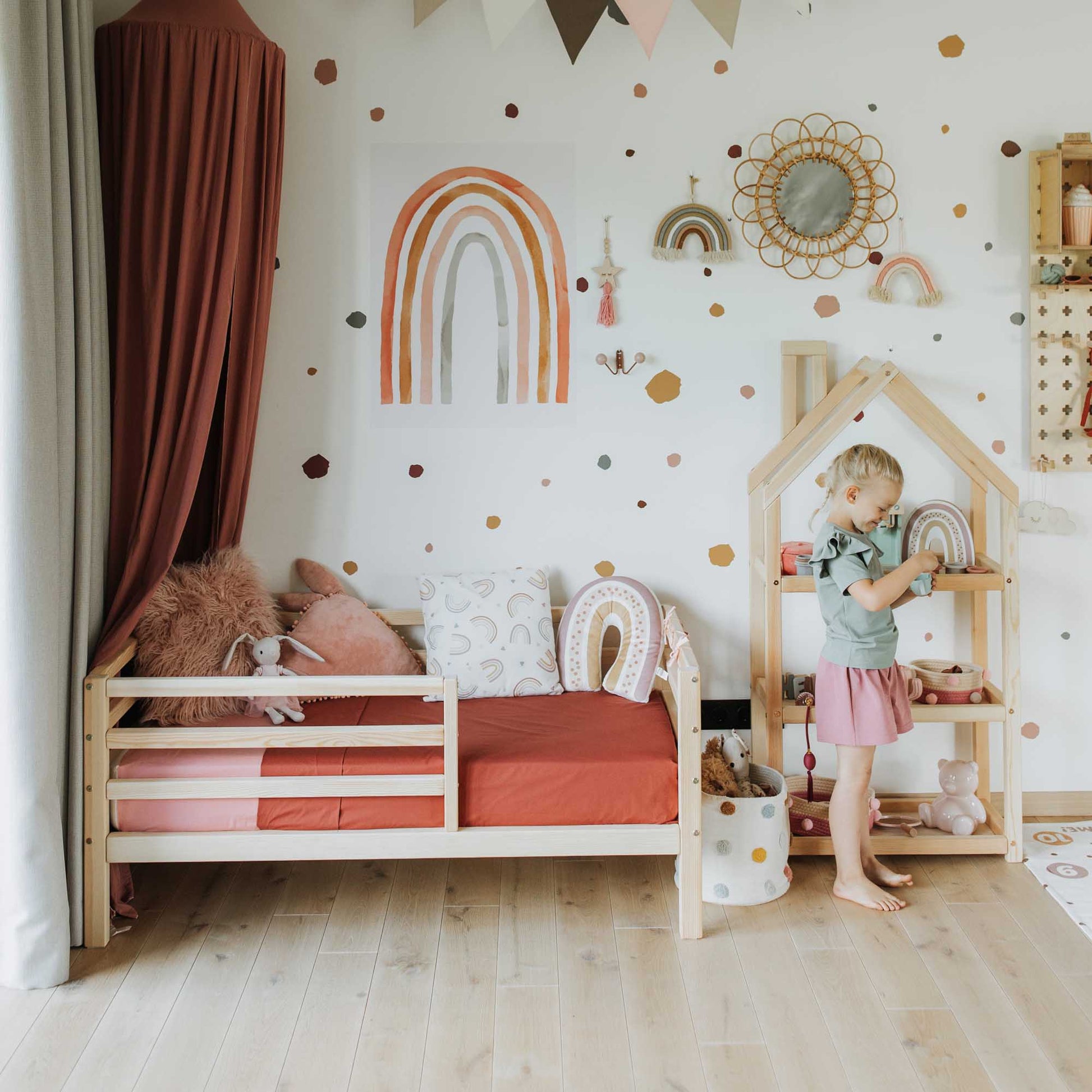 A little girl's room with a Sweet Home From Wood kids' bed on legs with a horizontal rail fence and polka dot walls.