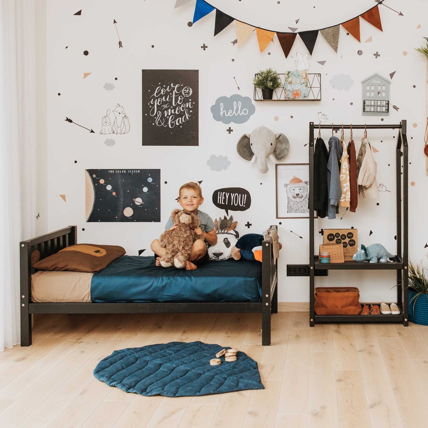 A Montessori-inspired child's room with a Sweet Home From Wood raised kids' bed on legs with a headboard and footboard, teddy bear, and stuffed animals.