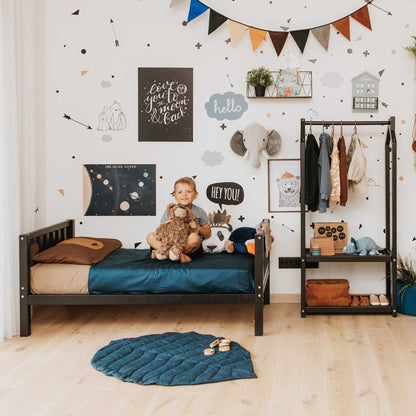 A child's room with a solid pine or birch wood 2-in-1 kid's bed on legs with a vertical rail headboard and footboard, teddy bear, and stuffed animals.