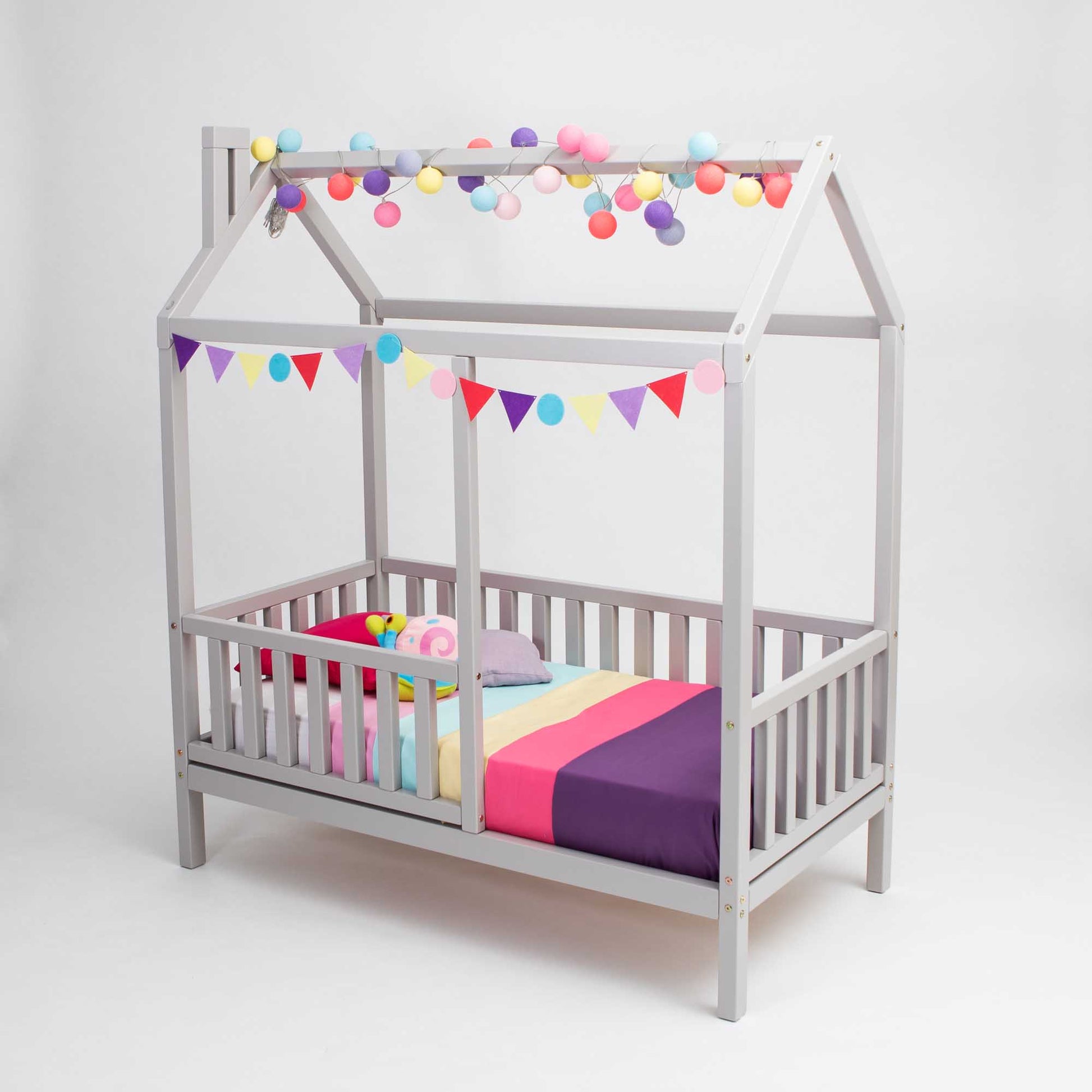 A Kids' house bed on legs with a fence with a colorful canopy and bunting.