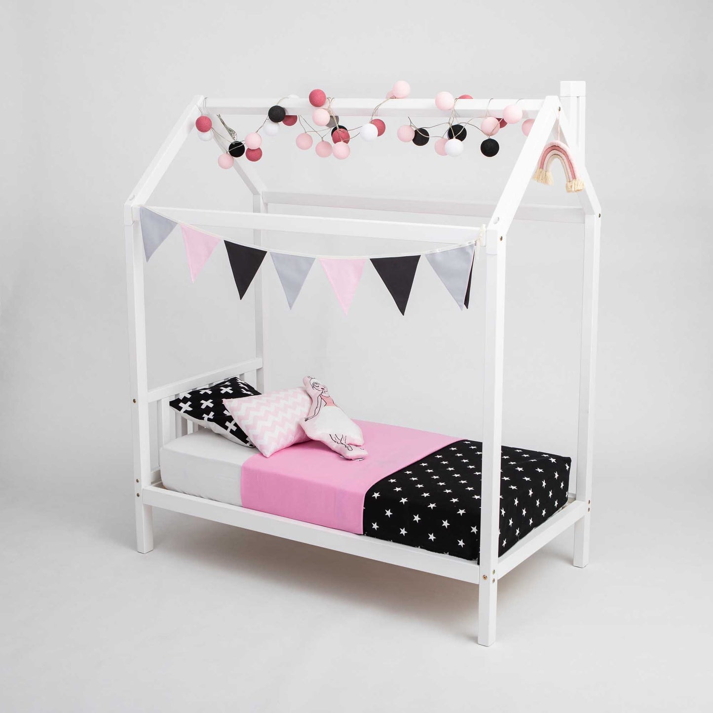 A Toddlers' house bed on legs with a headboard and a pink and black polka dot canopy and bunting.