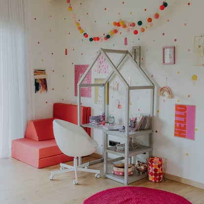 A girl's room with a desk, chair and polka dot walls. This charming space is complete with a Sweet Home From Wood House-shaped toddler desk and a comfortable chair. The playful polka