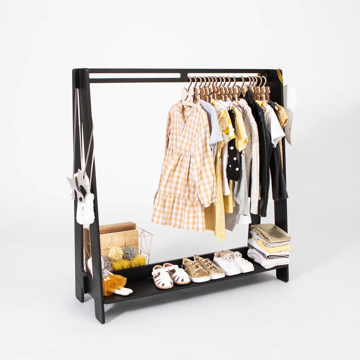 An open wardrobe with toddler clothing hanging on a black Kids' clothing rack from Sweet Home From Wood, creating a Montessori-inspired wardrobe setup.