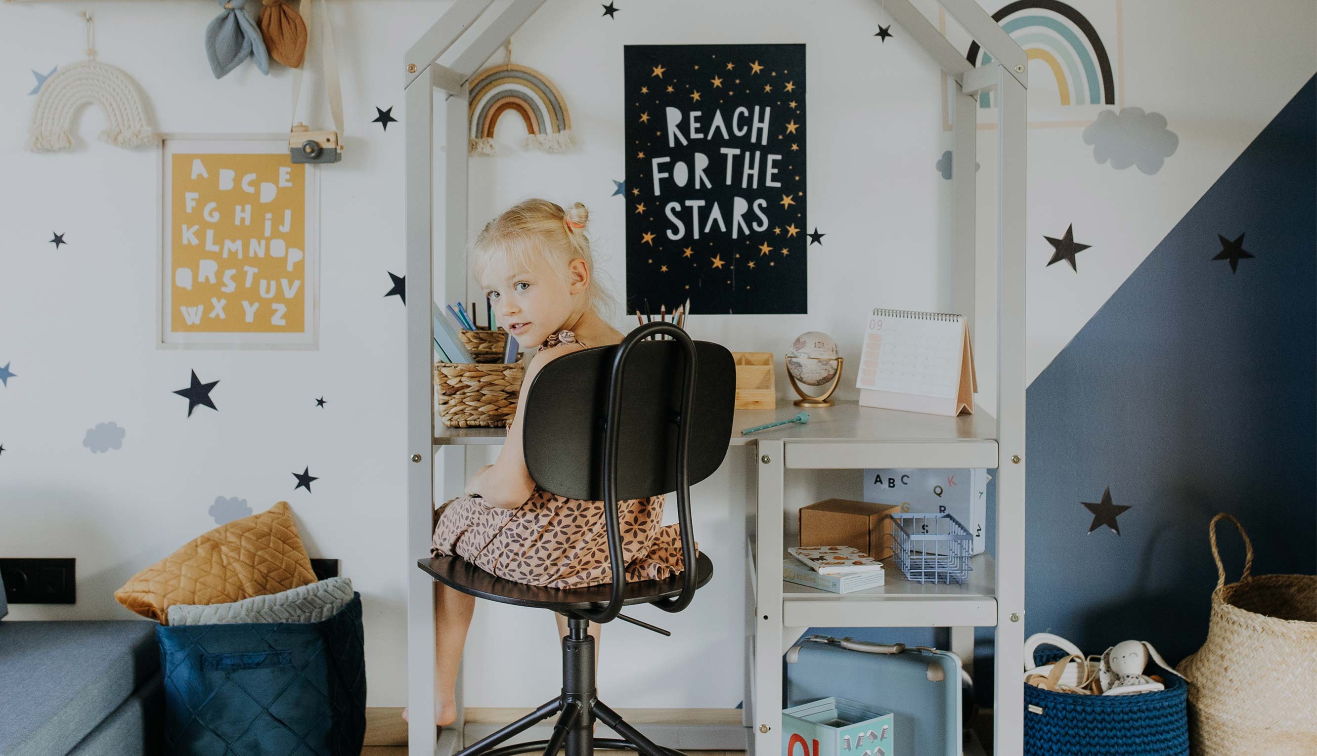 A little girl sits at a desk in a child's room.