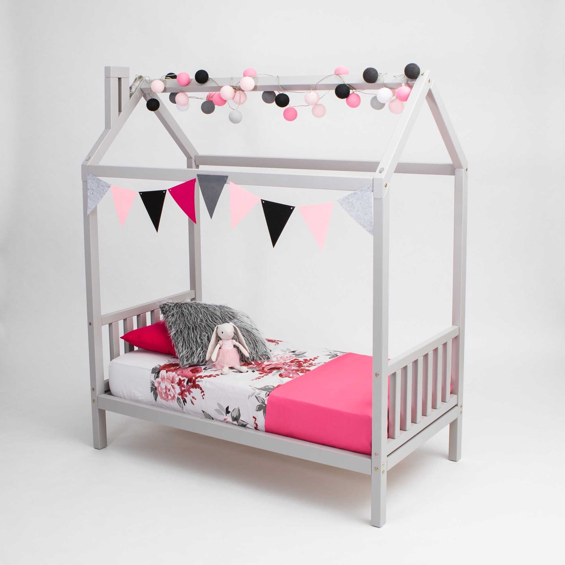 A girl's toddler house bed on legs with a pink and grey canopy and bunting.