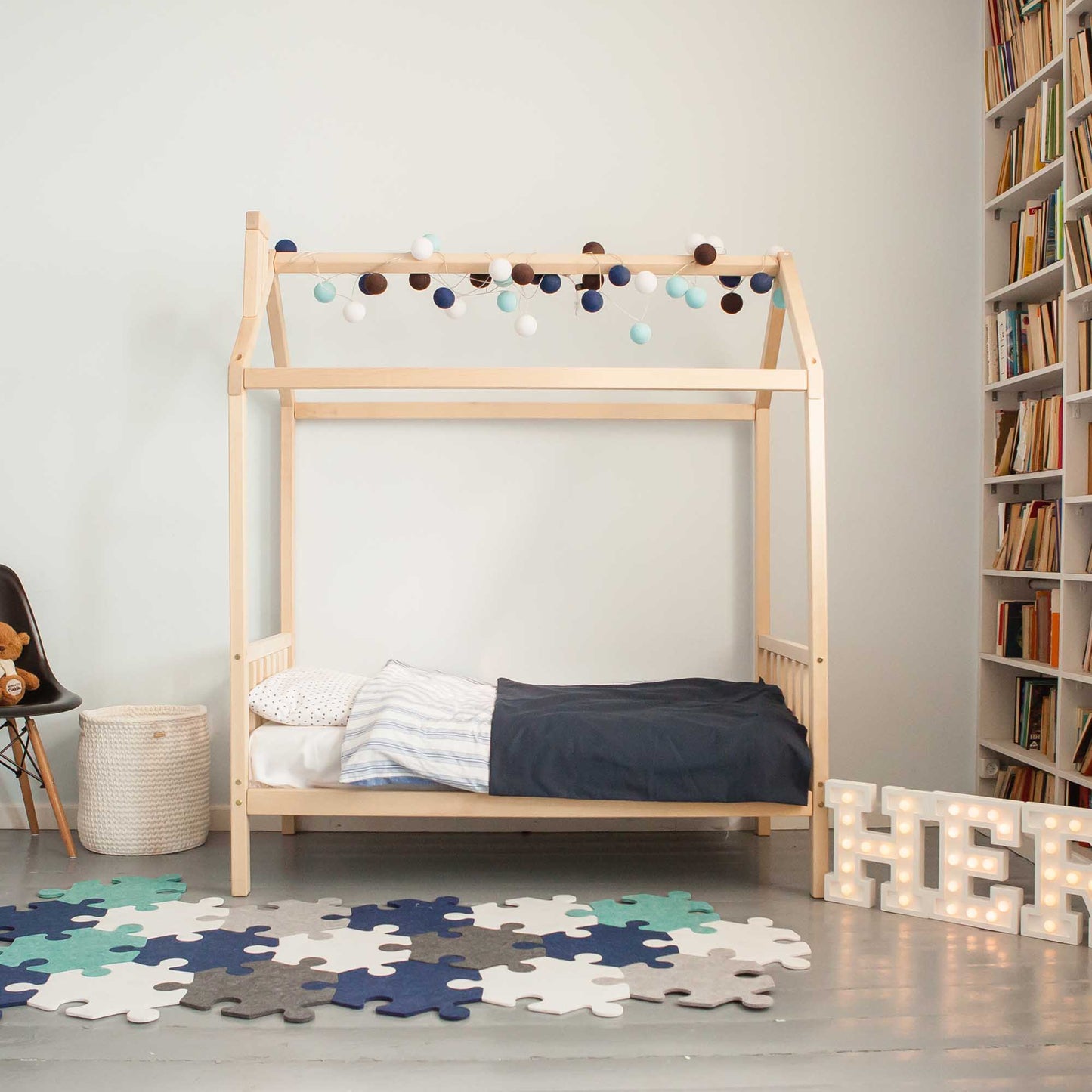 A child's room with a Toddler house bed on legs with a headboard and footboard and wooden bookshelves.
