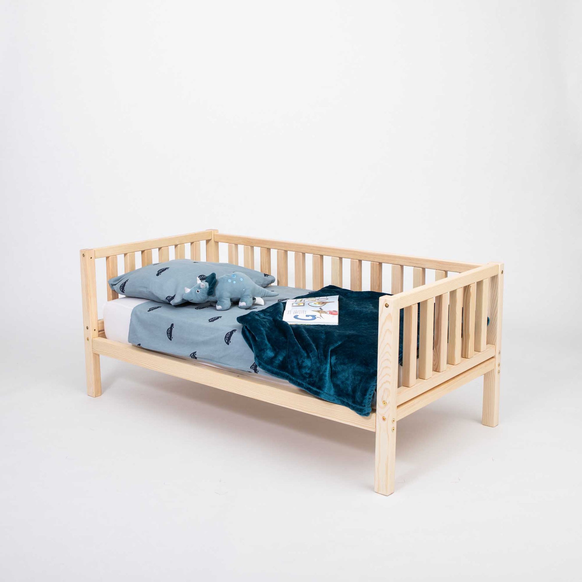 A Sweet Home From Wood Kids' platform bed on legs with 3-sided rails with a blue blanket on it.