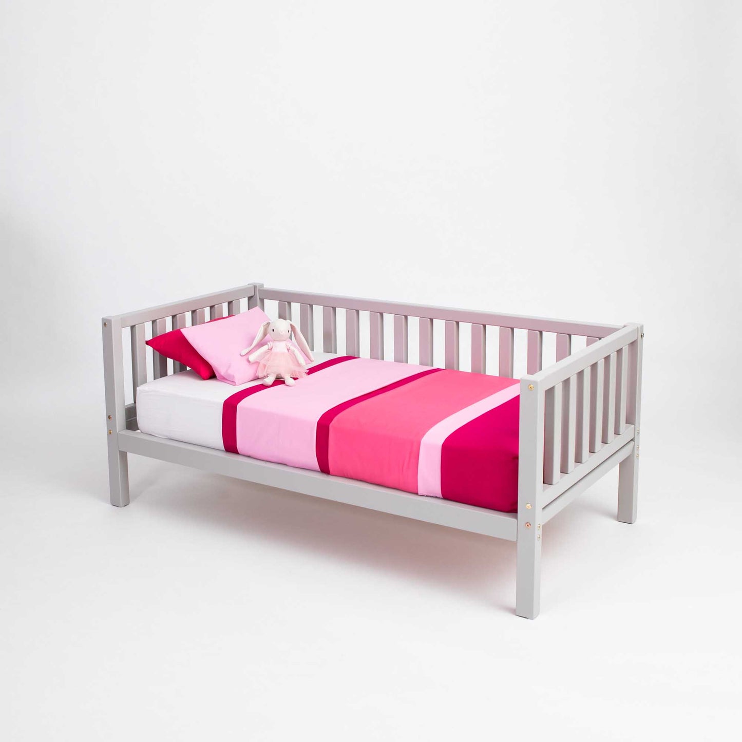 A Sweet Home From Wood 2-in-1 toddler bed on legs with a 3-sided vertical rail, with pink and white bedding, placed at floor level.