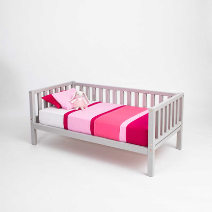 Montessori-inspired children's bed with pink and white bedding, known as the Kids' raised bed on legs with rails. A charming and secure sleep space.