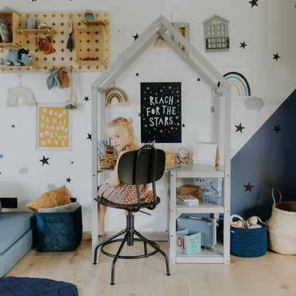 A little girl sits at a Sweet Home From Wood house-shaped toddler desk and chair set in a playroom.