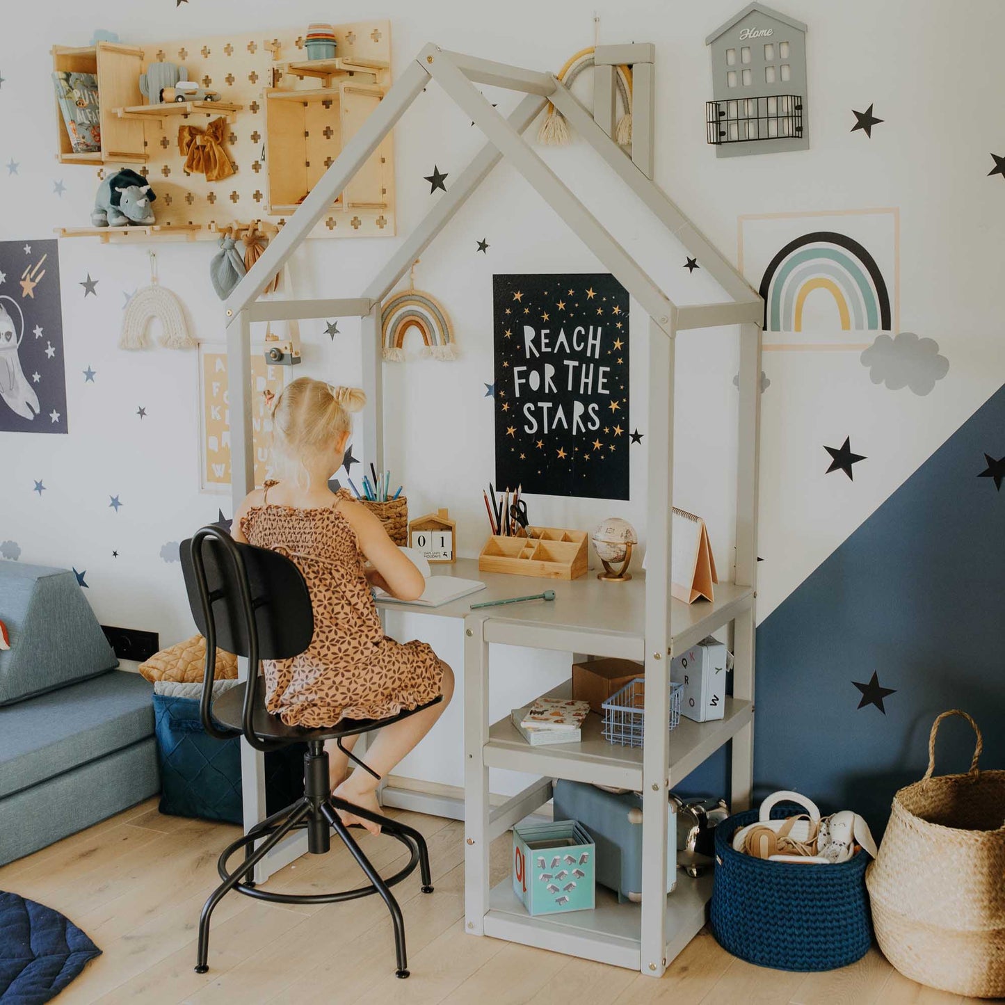 A toddler sits at a Sweet Home From Wood house-shaped toddler desk in a child's room.