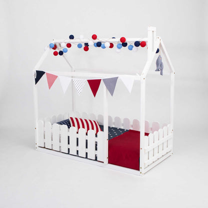 A white platform house bed with a picket fence and red, white and blue decorations.