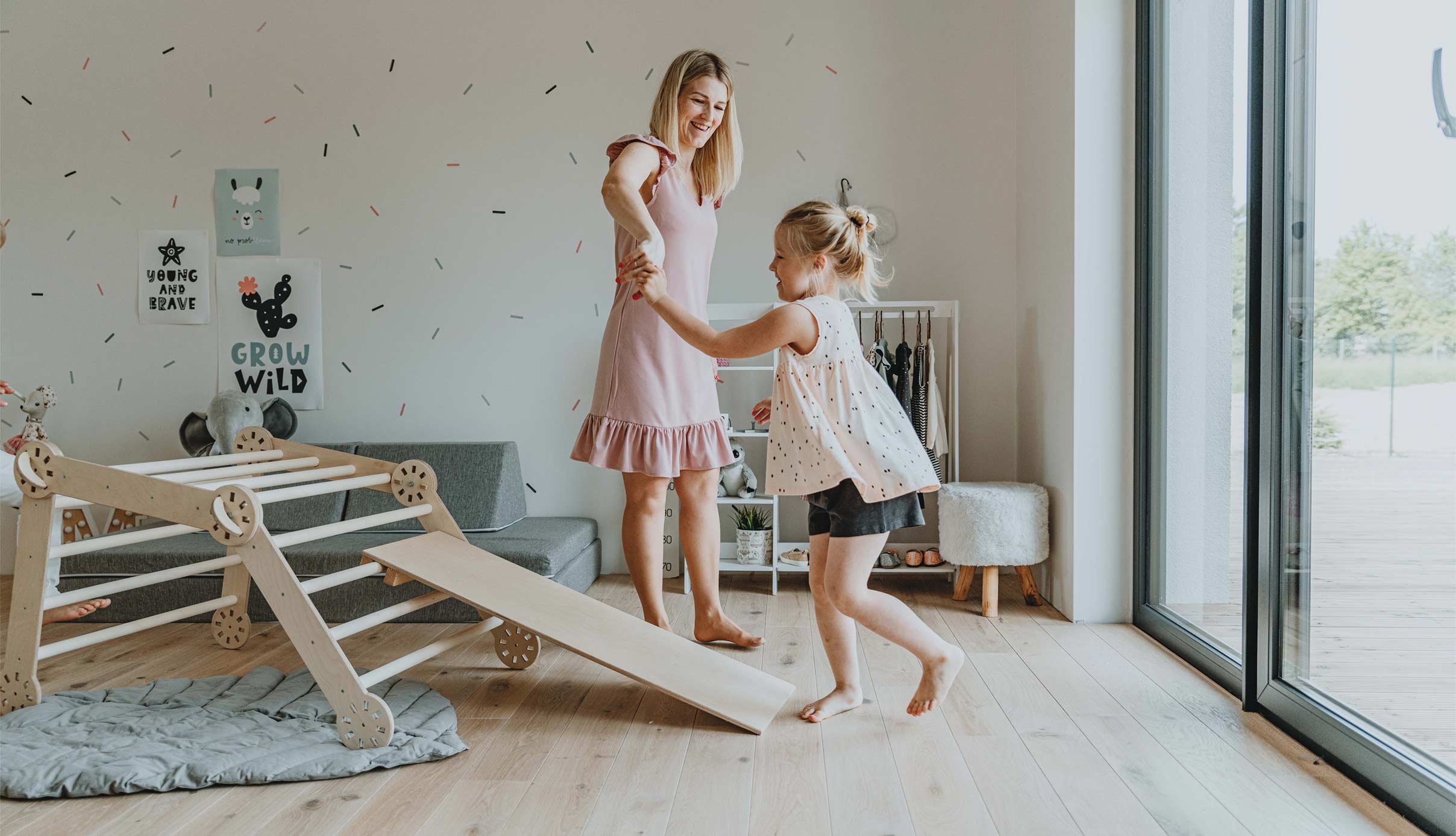 A mother and daughter playing in a room with a wooden play structure.