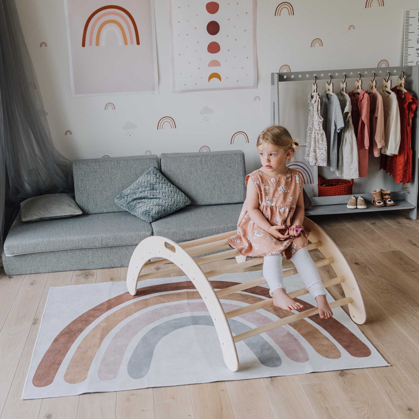 A little girl sitting on a rug in a room with Sweet Home From Wood's Climbing arch, Transformable climbing cube / table and chair, and a ramp.