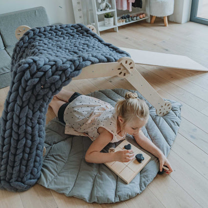A little girl laying on a blanket in a living room with a Transformable climbing triangle, Transformable climbing gym, and a ramp.
