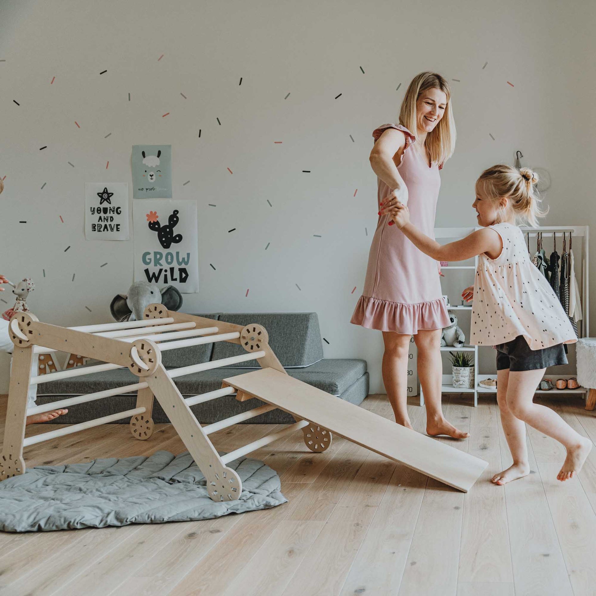 A woman and her daughter play with a transformable climbing gym in a living room.