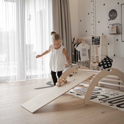 A little girl playing with a Sweet Home From Wood indoor climber, consisting of a Climbing arch, Transformable climbing cube/table and chair, as well as a ramp in her room.