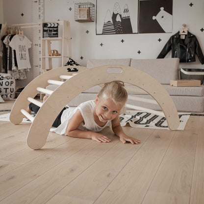 A little girl playing on the floor next to a wooden play structure and Sweet Home From Wood Climbing arch + Transformable climbing cube / table and chair  + a ramp.