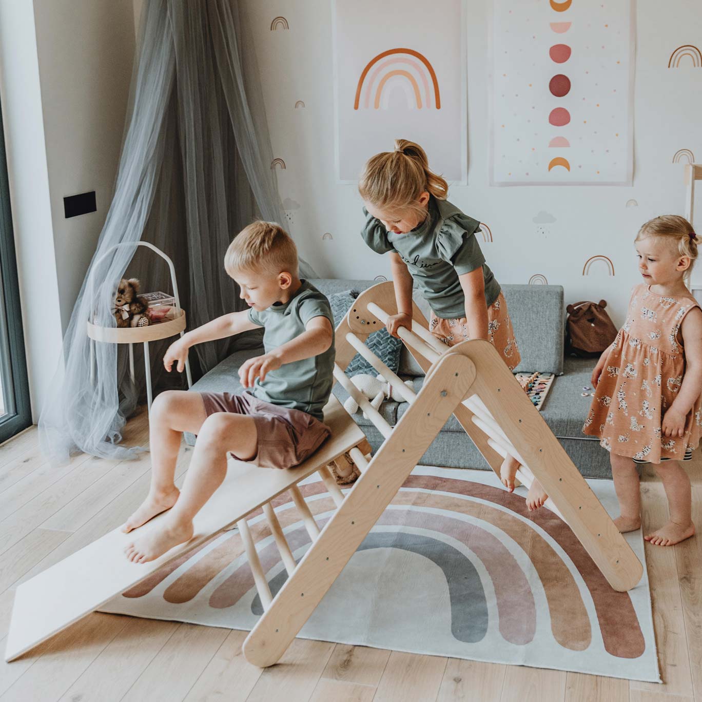 Three children playing on a wooden slide in a living room.