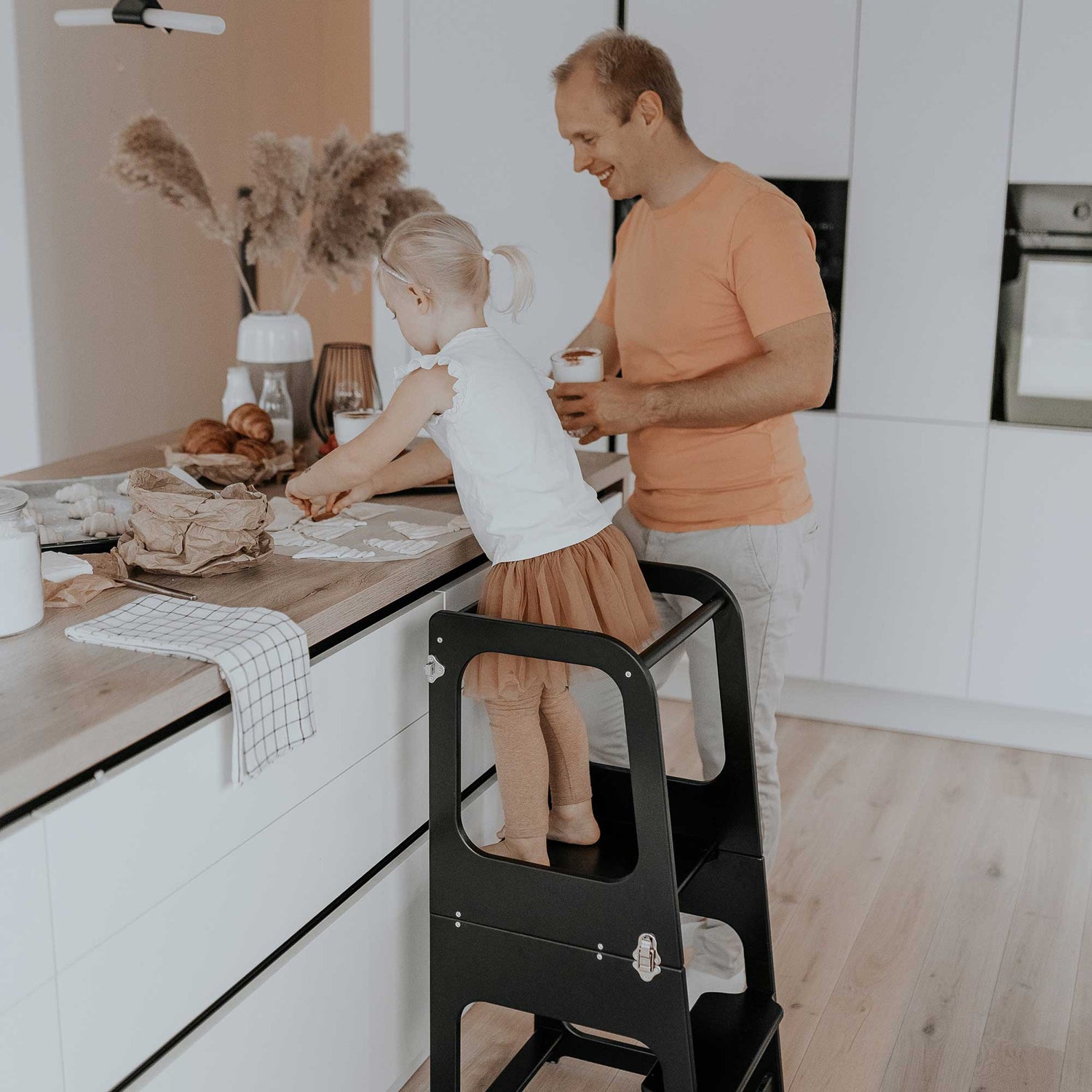 A man and a child standing on a step stool in a kitchen.