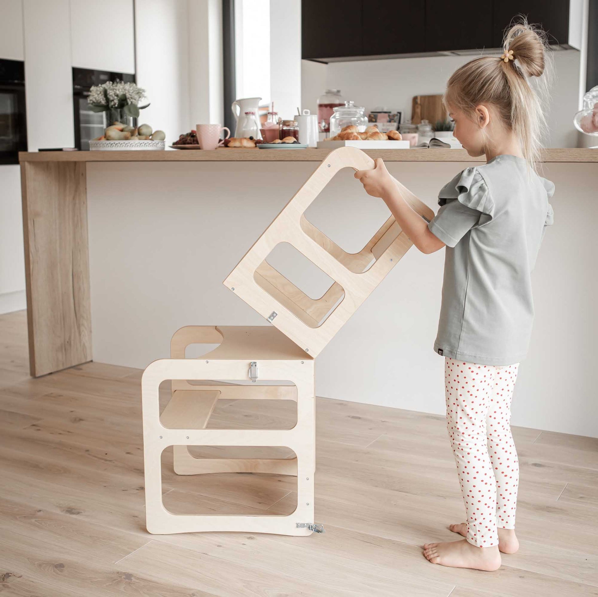 A toddler is playing with a Sweet Home From Wood 2-in-1 transformable kitchen tower - table and chair set.
