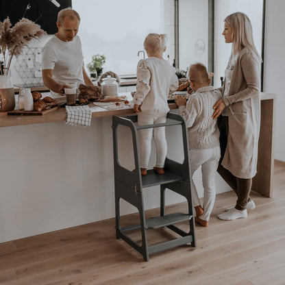 A family is in the kitchen with a child on a 2-in-1 Convertible kitchen tower - table and chair.