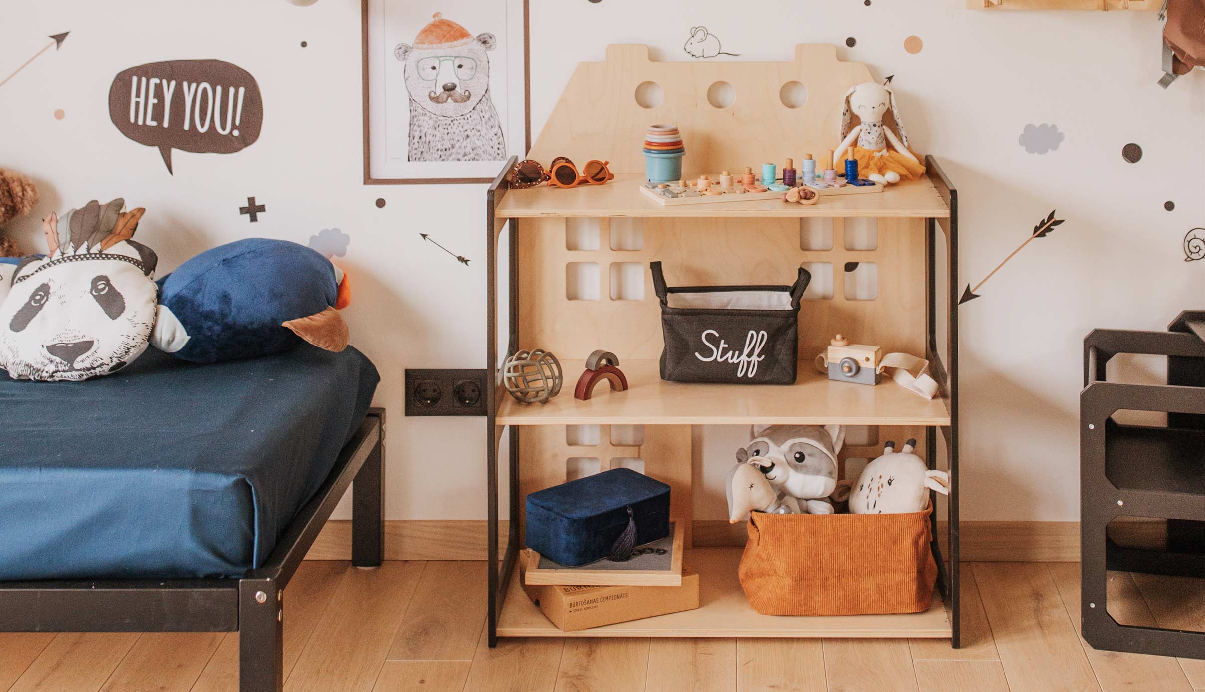 A child's room with a bed, bedside table, and stuffed animals.