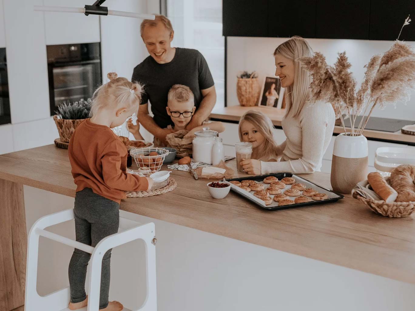 Family with a girl standing on a toddler step stool and cooking.