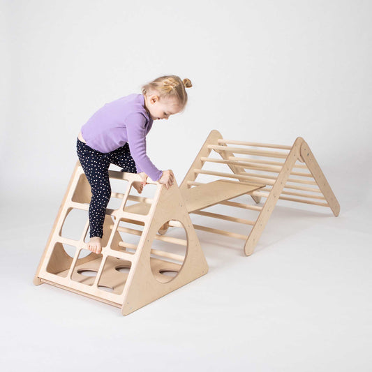 A little girl playing with a Sweet Home From Wood indoor climber play structure, which includes a Climbing triangle, Foldable climbing triangle, and a ramp.