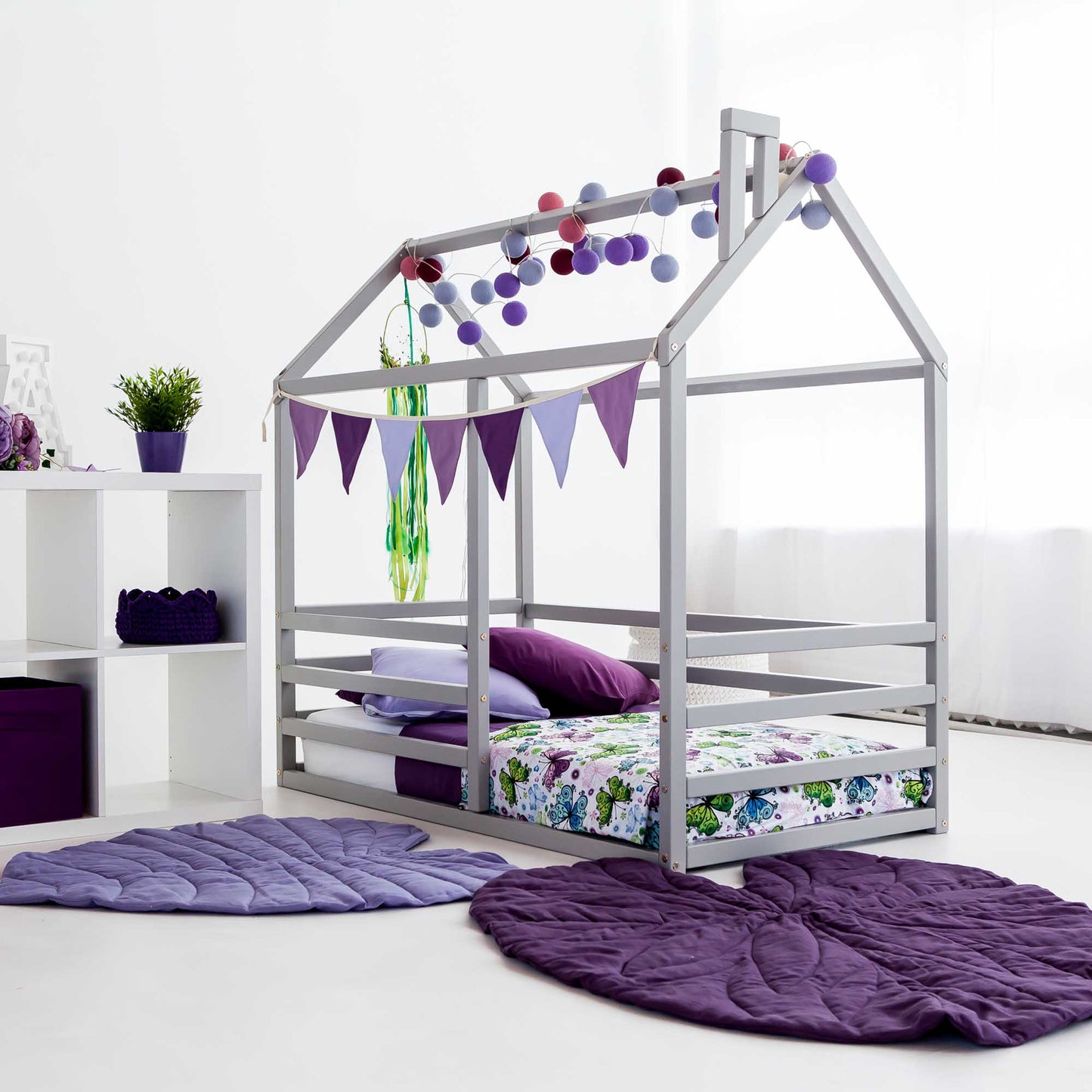 A child's room with a Floor level house bed with a horizontal fence and purple pillows.